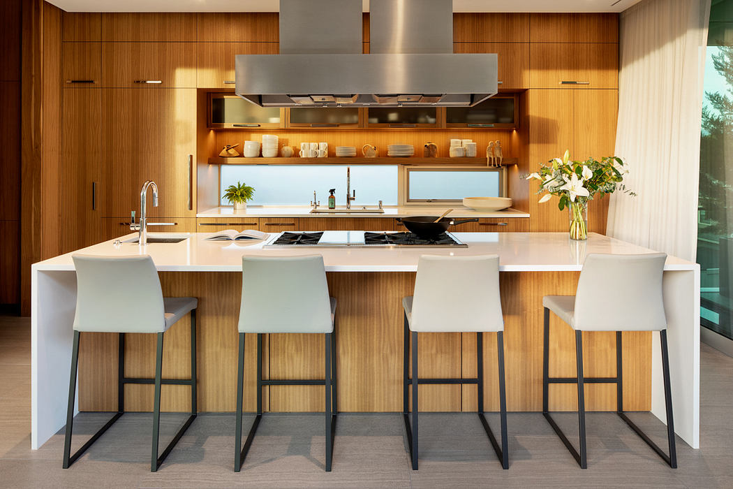 Sleek, modern kitchen with wooden cabinetry, island, and white counter stools.