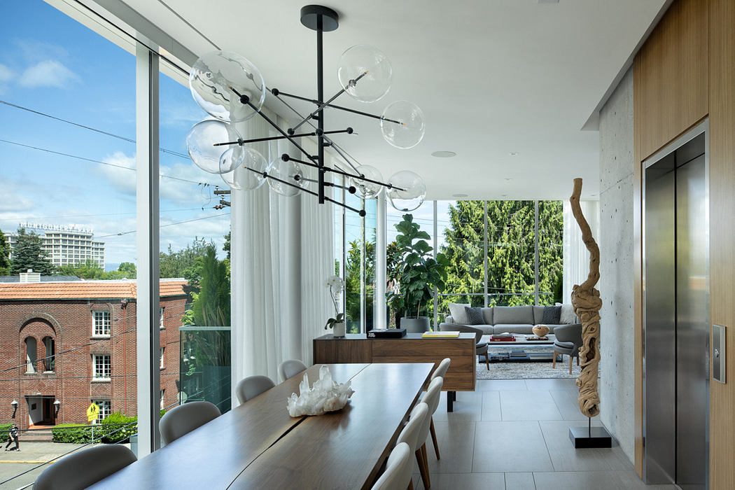 A modern, open-concept interior with a sleek dining area, stylish chandelier, and expansive windows overlooking greenery.