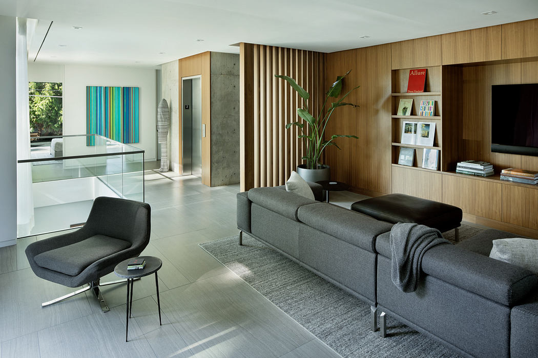 Spacious living room with wood paneling, gray couch, and a glass-enclosed staircase.