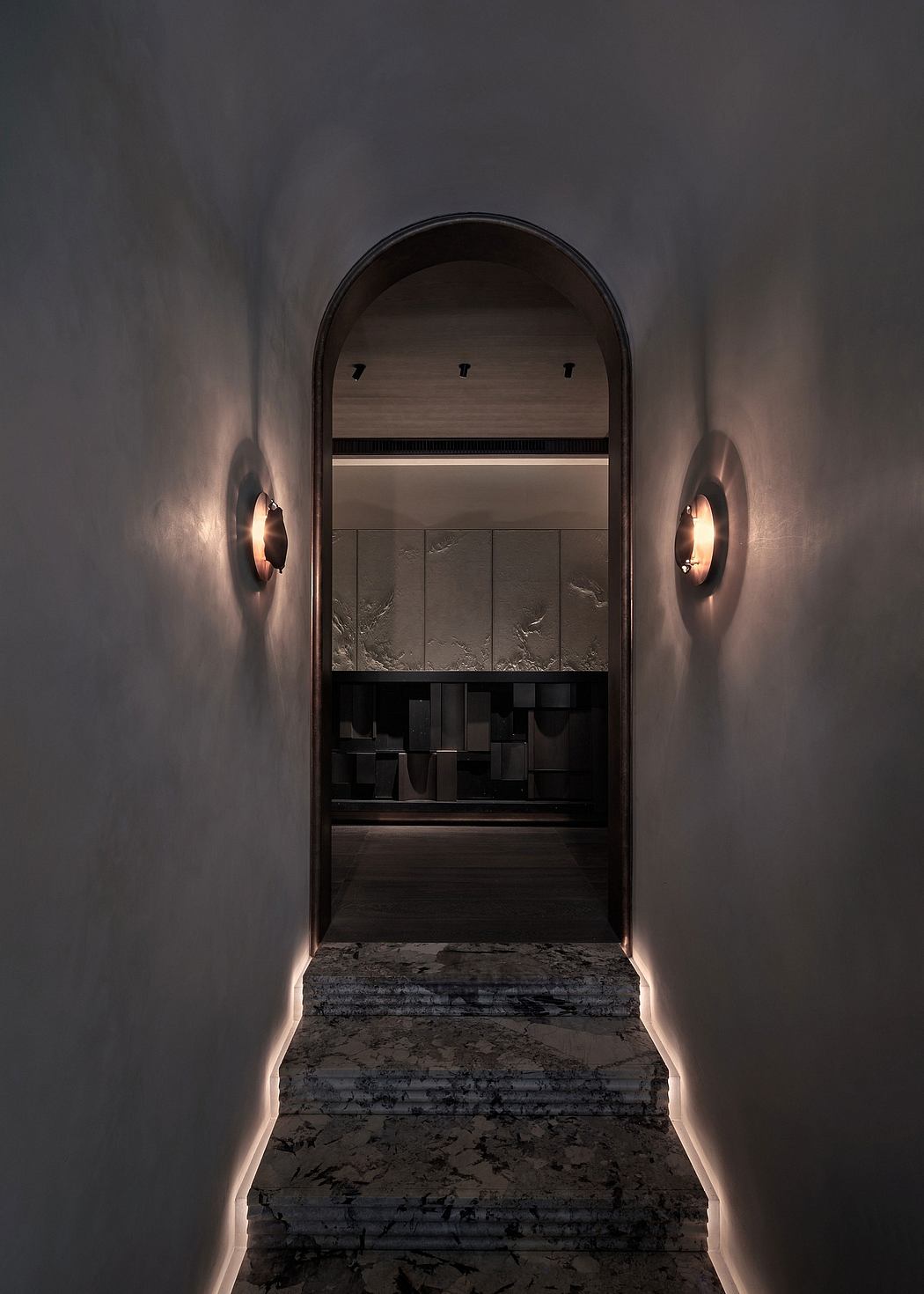 Dimly lit archway framing a modern built-in shelving unit, illuminated by wall sconces.