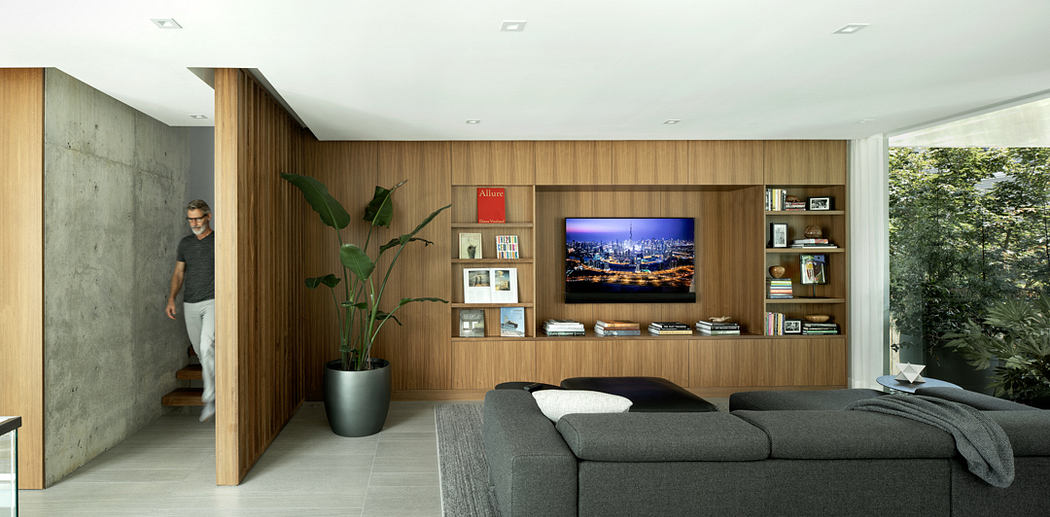 A modern living room with wooden wall paneling, built-in shelves, and large windows overlooking greenery.