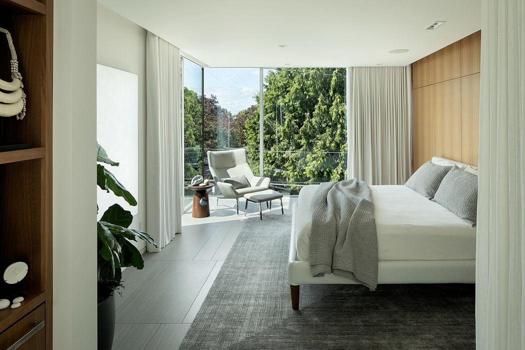 Spacious bedroom with wall-to-wall windows, plush furnishings, and verdant outdoor view.