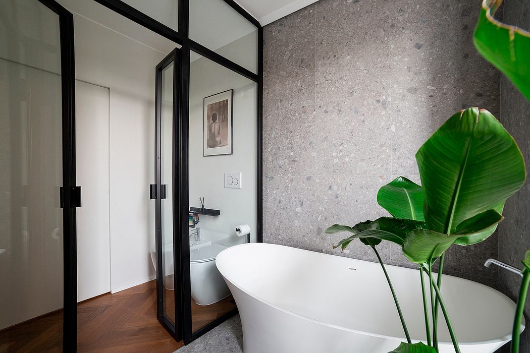 Modern bathroom with freestanding tub, black-framed glass walls, and tropical plant accent.