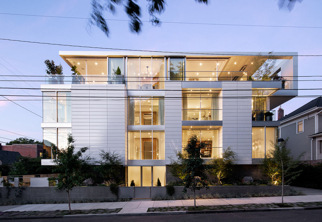 Contemporary multi-story building with sleek glass and metal facade, illuminated interiors.