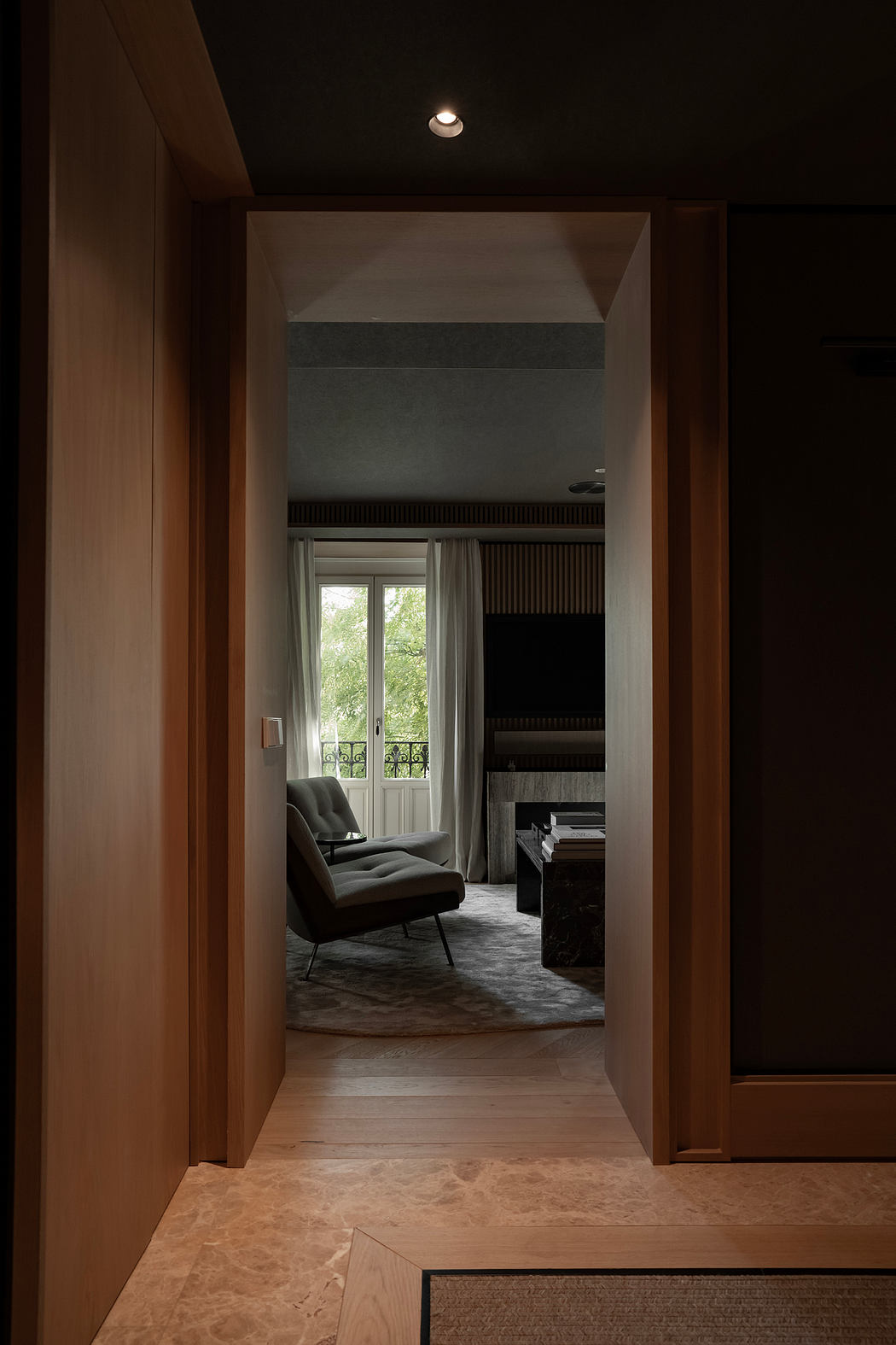 A cozy living room with wooden panels, a plush armchair, and a window overlooking nature.